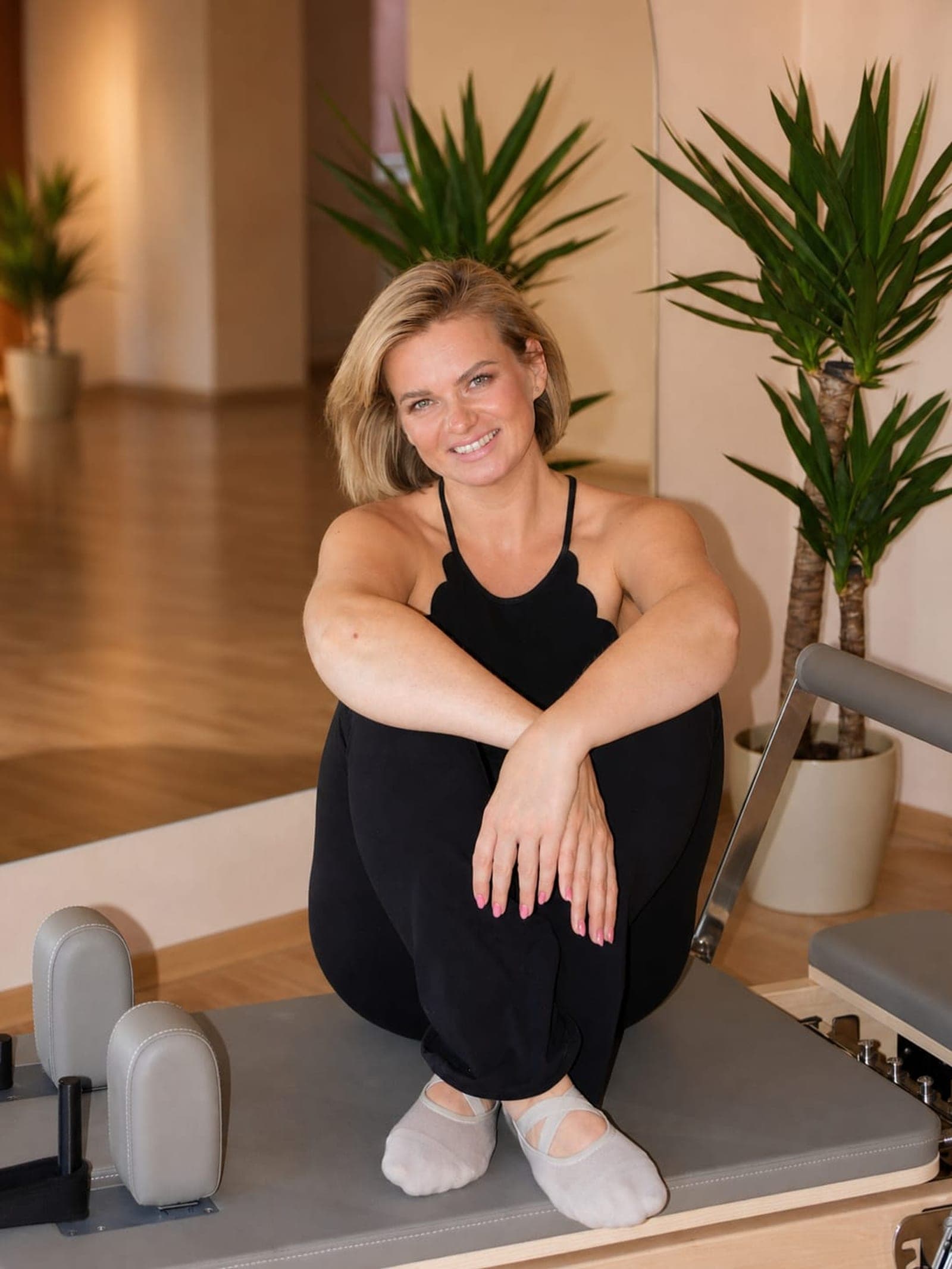 Lektorka Lenka Ligocká sedí na reformeru s rukama složenými na kolenou, studio Axis Pilates