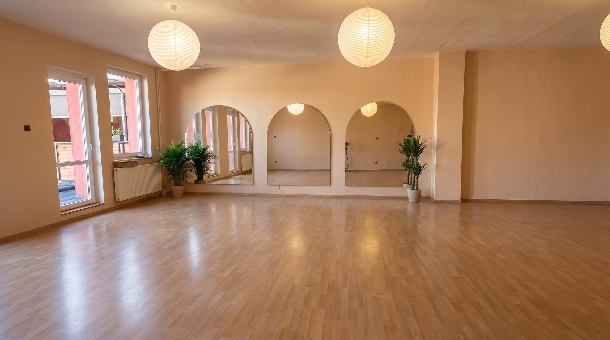 Prázdný světlý sál Axis Pilates s dřevěnou podlahou, okny na náměstí a zrcadlovými oblouky